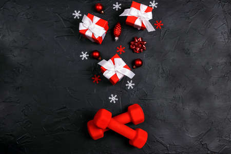 Red dumbbells with winter decorations on black background. Top view, flat lay Christmas fitness composition.の写真素材