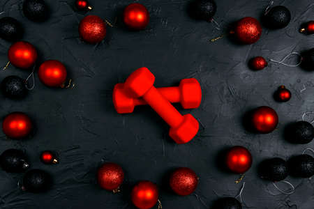 Red dumbbells with Christmas balls on black background. Top view, flat lay Christmas fitness composition.の写真素材
