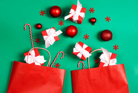 Two red paper shopping bags with Christmas decorations and gift on green background with copy space...