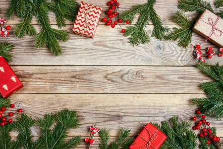 Christmas frame made of fir branches, berries and gifts on wooden background. Copy space, top view.の写真素材