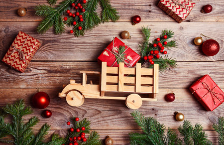 Wooden toy truck with gift box, fir branches and Christmas decorations on wooden background. Top-down composition.の写真素材