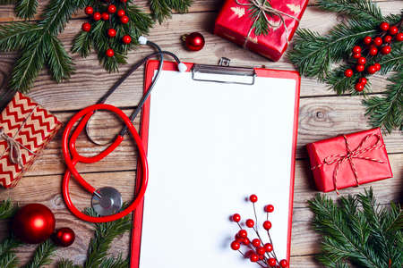 Stethoscope and blank tablet with Christmas decorations, gifts and fir branches on wooden background. Christmas greeting card for medics concept. Copy space for text.の写真素材