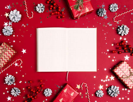 Blank notepad surrounded by Christmas decorations and gifts on a red background. Wish list and goals, schedule and diary.の写真素材