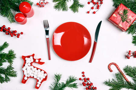 Christmas festive table setting with red dish, cutlery, gift, decorations and fir branches on white table. Top view.の写真素材
