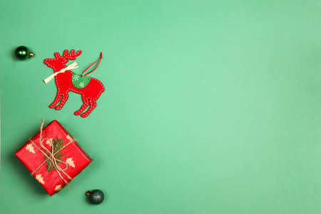 Green Christmas background with red gift and decoration deer. Copy space, top view.