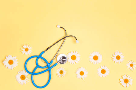 Blue stethoscope with chamomile flowers on yellow background. Top view with copy space. National Doctor's day. Happy nurse day.の写真素材