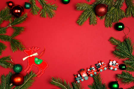 Christmas frame made of fir branches and toys decorations on a red background. Copy space, top view,...