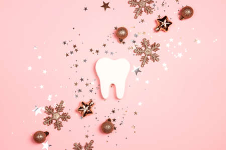 White tooth with gold decorations on pink background. Dentist Merry Christmas and New Year concept. Top view, flat lay.の写真素材