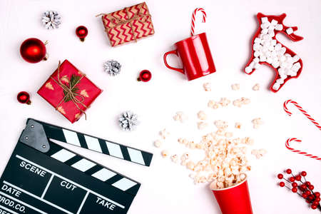 Movie clapper board with Christmas decorations and gifts, popcorn, mug and marshmallow on white background. Cozy leisure time with a movie during the winter holidays.の写真素材