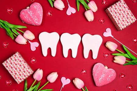 White teeth surrounded by gifts, hearts and tulip flowers on a red background. Dental Valentine...