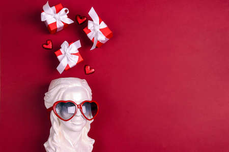 White female plaster head with heart shaped glasses on the eyes and gifts overhead on red background. copyspace. Romantic and love, Valentine's Day concept.の写真素材