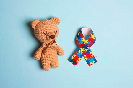 Autism concept with toy bear and puzzle awareness ribbon on a blue background. Autism Awareness Day. Autism Spectrum Disorder (ASD) concept.の写真素材