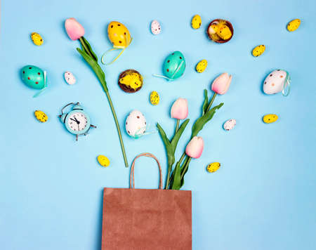 Brown paper shopping bag with Easter decorations and tulips on blue background. Easter sales and discounts.の写真素材