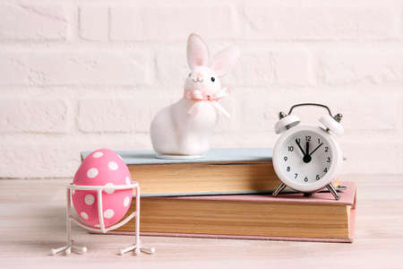 Easter background with books, egg, rabbit and alarm clock against a white brick wall. Copy space for text.の写真素材