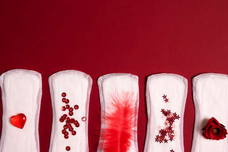 Sanitary napkins with different red items of them on red background. Menstruation cycle period, woman hygiene concept.の写真素材