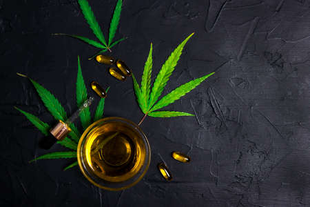 Bowl with CBD oil, a dropper, capsules and marijuana leaves on black background. Beauty care with hemp oil concept.の写真素材