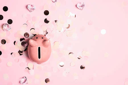 Piggy bank on pink background with paper confetti and crystals. Saving money concept.