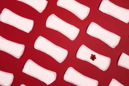 Sanitary napkins with red gift bow on one of them on red background. Menstruation cycle period, woman hygiene concept.の写真素材