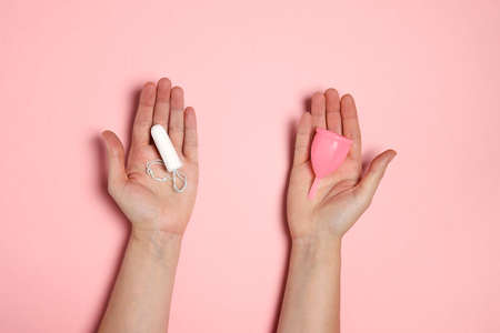Female hands holding pink silicone menstrual cup and cotton tampon for critical days. Choice of feminine hygiene products. Zero waste and healthy lifestyle concept.の写真素材