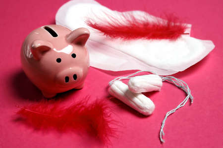 Sanitary tampons and pad with piggy bank on pink background. Spending, discounts, savings on feminine hygiene products.の写真素材