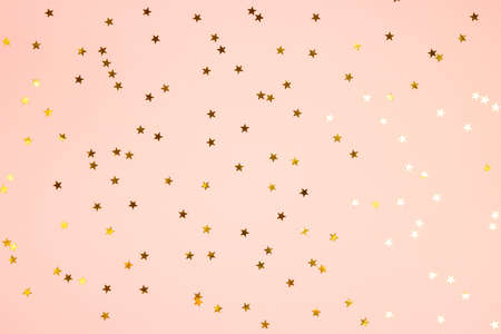 Golden star shaped glitter confetti on pink background. Festive flat lay holiday pastel backdrop....
