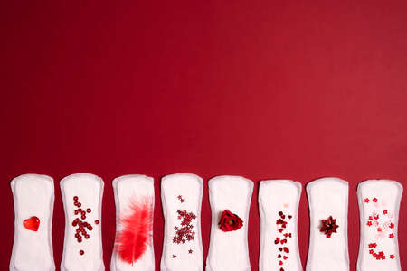 Sanitary napkins with different red items of them on red background. Menstruation cycle period,...