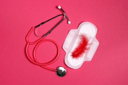 Stethoscope and sanitary napkin with red feather on it on pink background. Women's health, menstruation cycle period,の写真素材