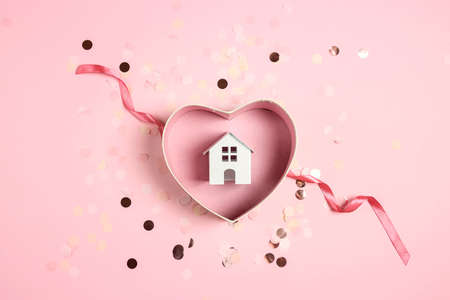 House model in heart shaped gift box with ribbon on a pink confetti background. Buying, giving, celebrating.の写真素材