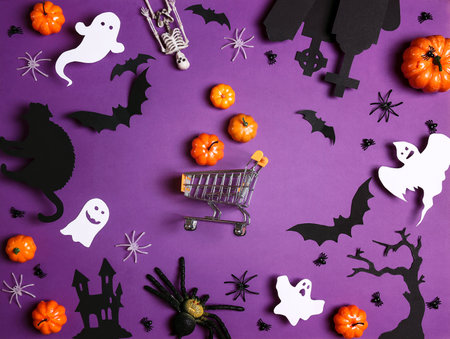Miniature shopping cart with Halloween decorations on purple background. Holiday shopping and sale.の写真素材
