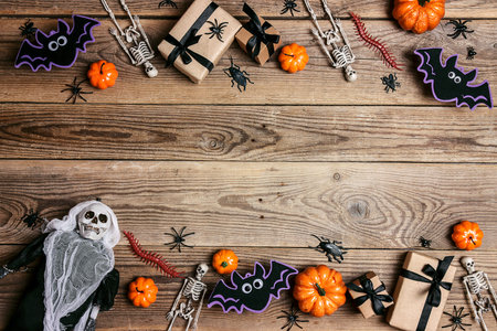 Halloween border with gifts, pumpkins, spiders, skeletons and bats on the old wooden boards. Top view rustic background with copy space.の写真素材