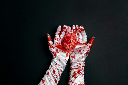 Creepy human brain in hands in bloody gloves on a black background. happy halloween party.の写真素材