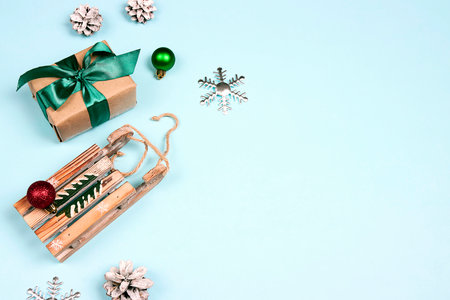 Gift box with wooden toy sled and Christmas baubles on a blue background. Flat lay border with copy space.の写真素材