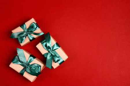 Gift boxes with green ribbons on a red background. Flat lay border with copy space.