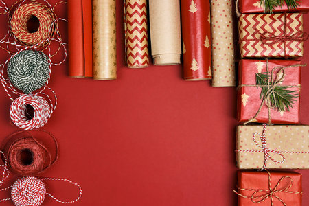 Christmas preparations with gift boxes, wrapping paper rolls and coils of rope on red background. Gifts packaging with copy space.の写真素材