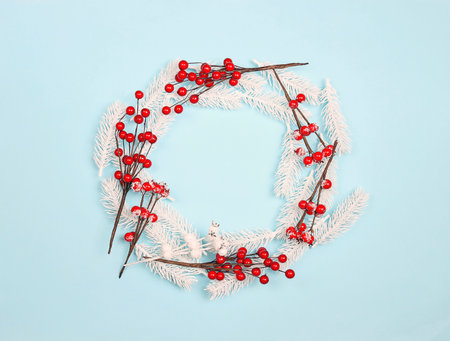 Festive round frame from white fir branches and red berries on blue background. Copy space, top view.の写真素材