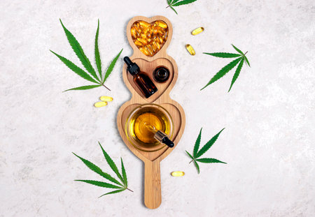Wooden heart dish with glass bottles with cbd oil, capsules and hemp leaves on light marble background. Top view, flat lay. alternative medicine.の写真素材