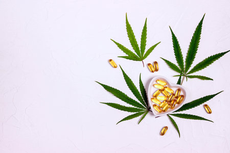 CBD oil capsules in heart saucers and marijuana leaves on white background. Top view, flat lay, copy space. alternative medicine.の写真素材