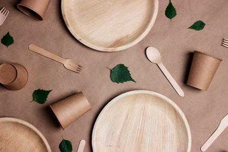 Set of different eco-friendly tableware with green birch leaves on brown paper background. Bamboo plates, paper cups and wooden cutlery. Zero waste, plastic free, biodegradable, disposable tableware. top view.の写真素材