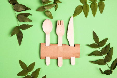 Set of Eco friendly bamboo cutlery with green foliage on green background. Disposable tableware, plastic free, zero waste concept. Flat lay, top view, copy space.の写真素材