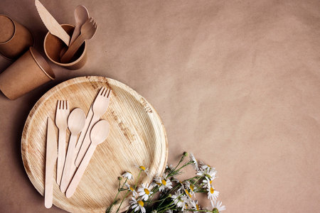 Set of eco-friendly tableware with bouquet of daisies on brown paper background. Bamboo plates, paper cups and wooden cutlery. Zero waste, plastic free, biodegradable, disposable tableware. top view.の写真素材