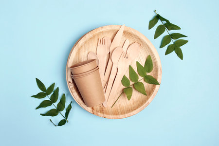 Set of different eco-friendly tableware with green leaves on blue background. Bamboo plates, paper cups and wooden cutlery. Zero waste, plastic free, biodegradable, disposable tableware. top view.の写真素材