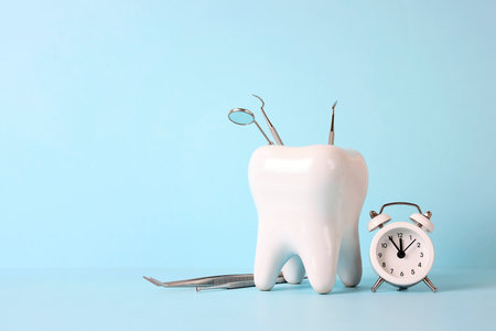 White human tooth with medical instruments and alarm clock on blue background. Time to dental health. Dentist day concept.の写真素材