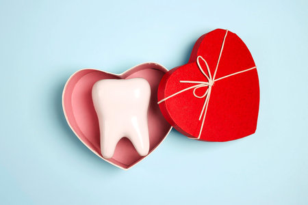 White tooth model in a heart-shaped box on a blue background. Dental treatment concept. Dental...