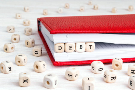 Word Debt written in wooden blocks in red notebook on white wooden table. wooden abc.の写真素材