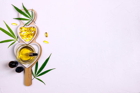 Heart dish with glass bottles, bowl with cbd oil, capsules and hemp leaves on white background. Top view, flat lay, copy space. alternative medicine.の写真素材