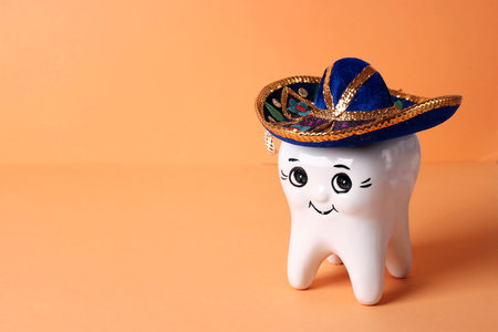 Cute happy smiling funny tooth with carnival hat on orange background. Copy space for space.の写真素材