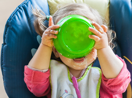 Little girl's eating mash and playing with his plateの写真素材