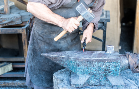 The blacksmith forging the molten metal on the anvil in smithy.の写真素材
