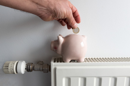 Savings concept. Piggy bank and money on heating radiator with temperature regulator