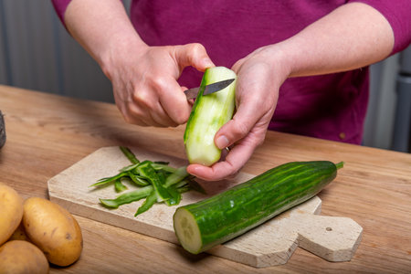 Woman peeling a cucumber in her kitchenの写真素材